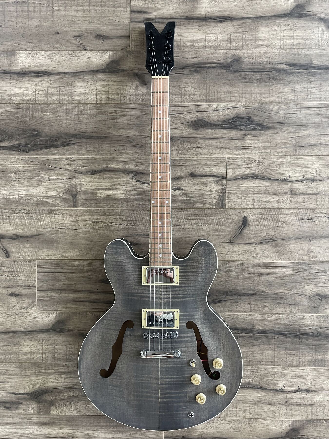 Semi-hollow double-cutaway guitar with a grey flame maple top, f-holes, white binding and two humbuckers