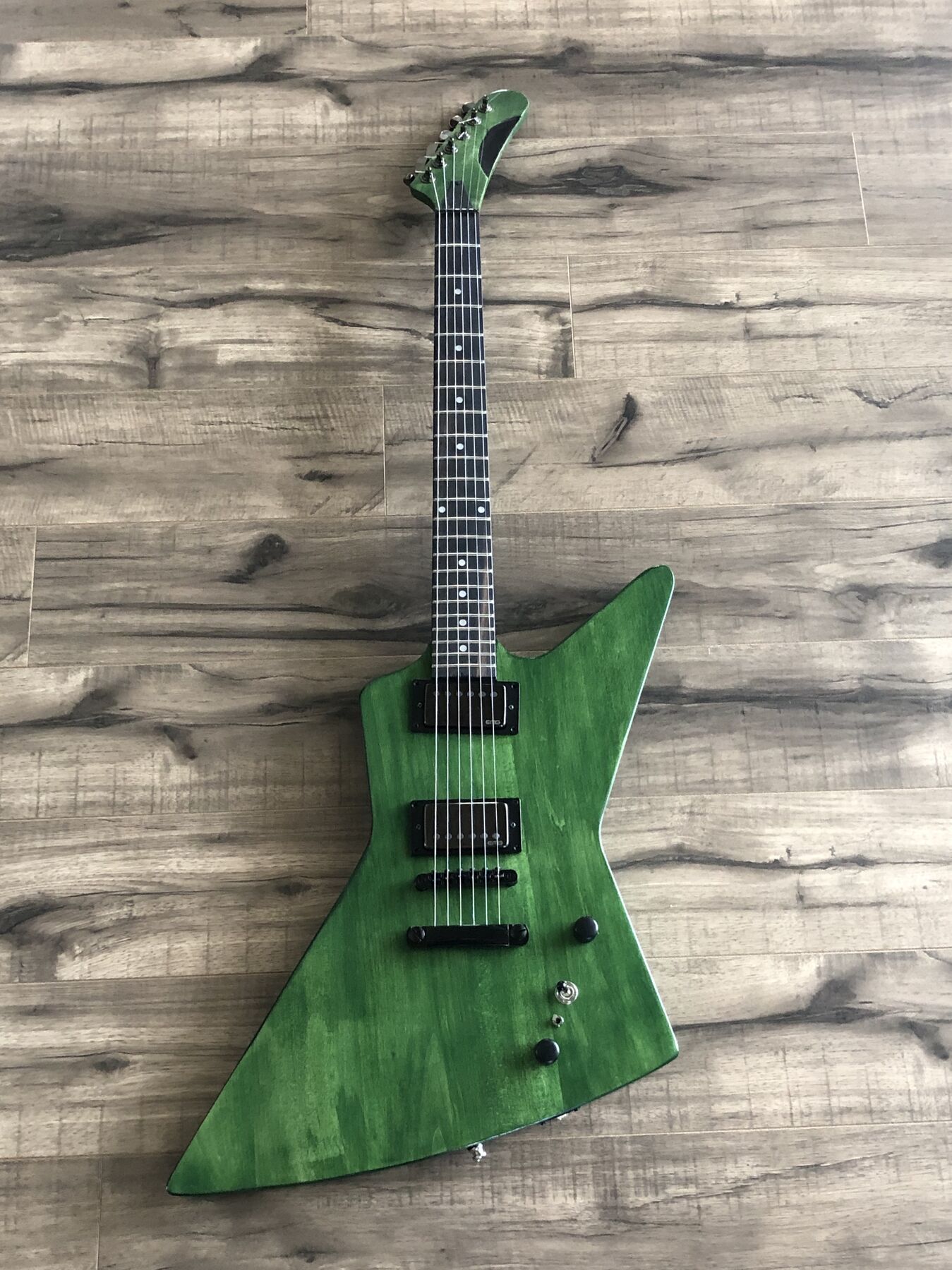 Green-stained offset guitar with black hardware on a wood floor