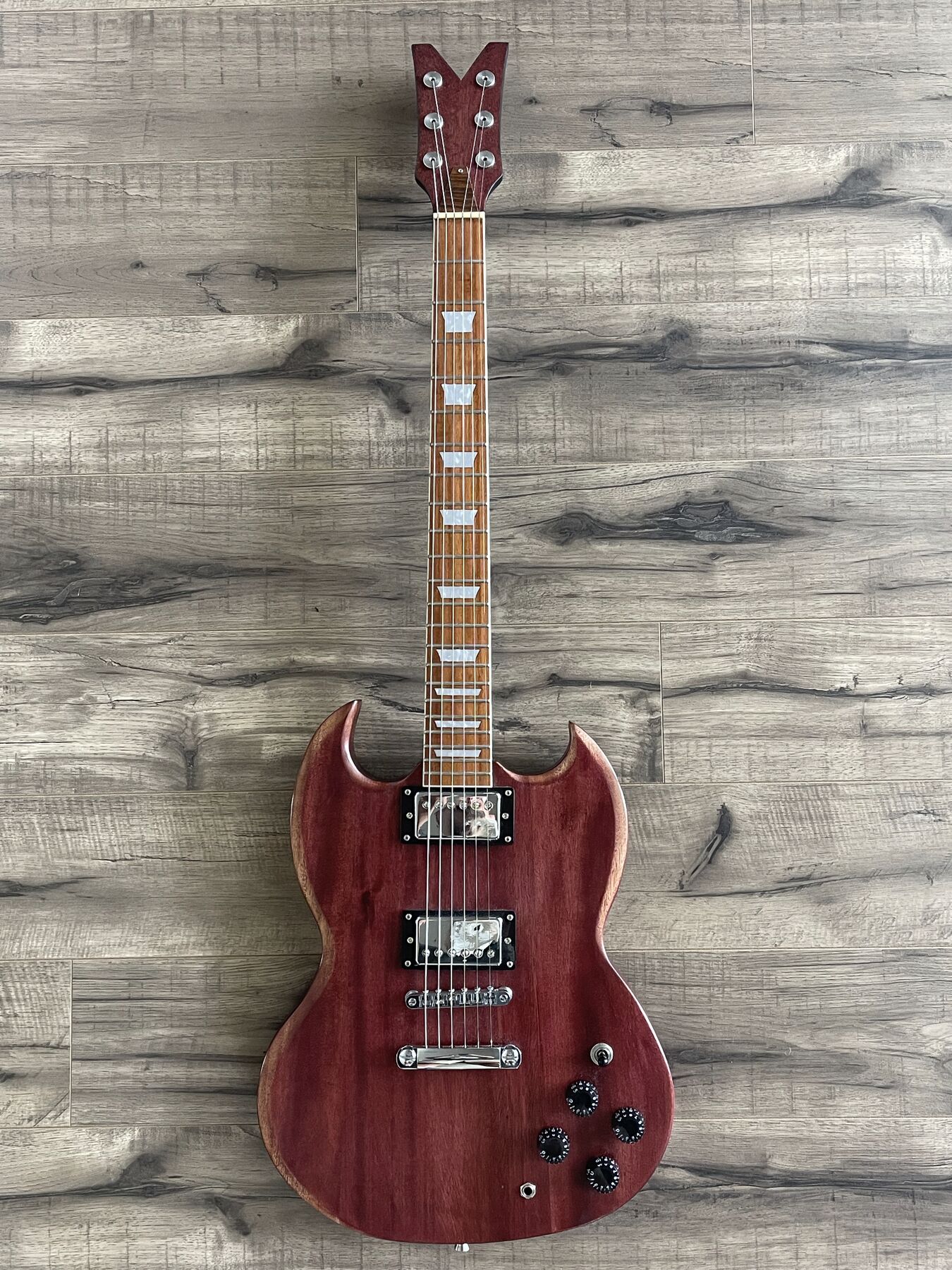 Red-stained double-cutaway guitar with pointed horns, a V-shaped headstock and two humbuckers