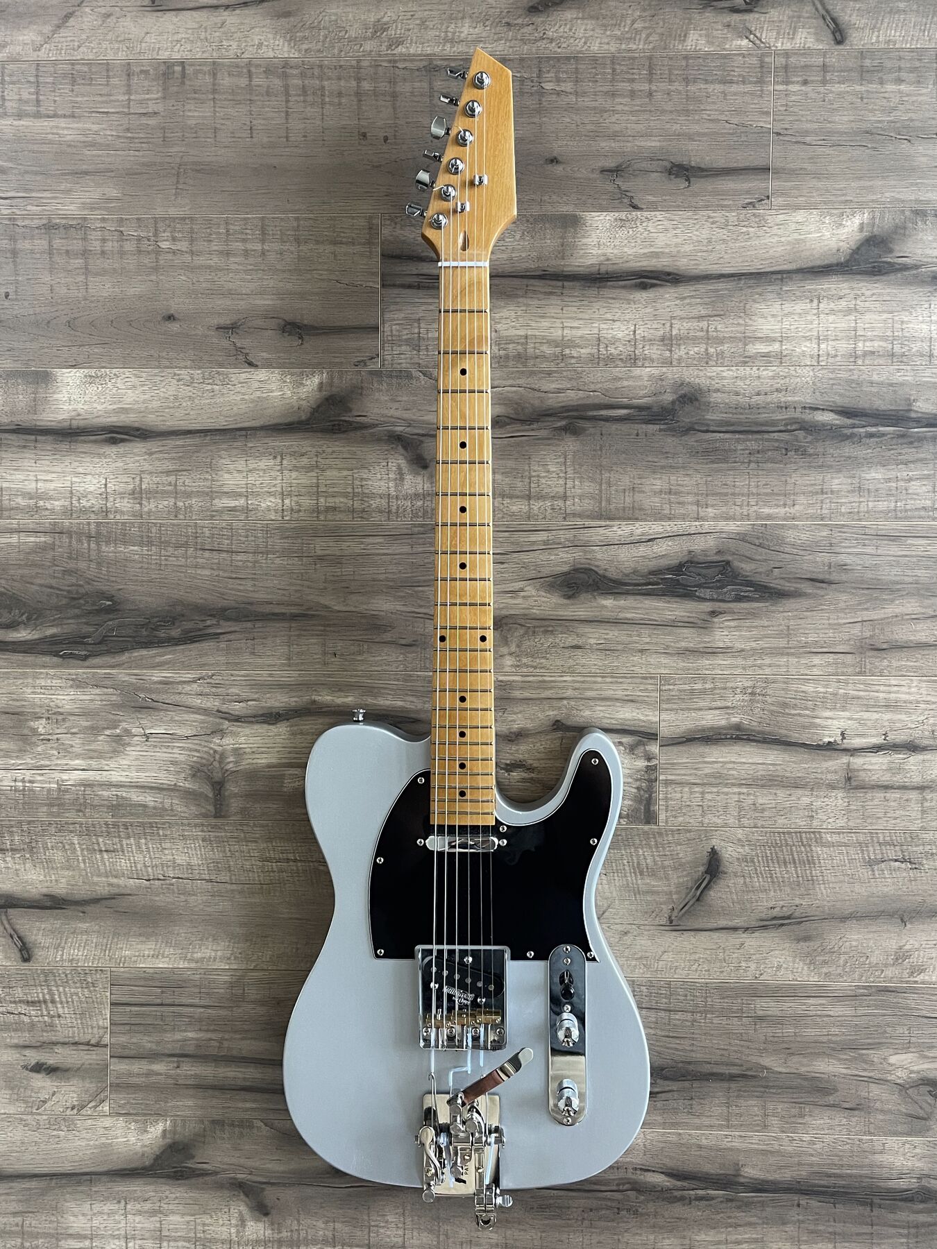 Silver single-cutaway guitar with a black pickguard, maple neck and a string bender at the tail